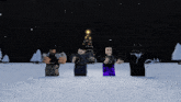 a group of people standing in the snow with a christmas tree behind them