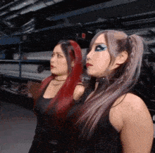 two women with red hair and purple hair are standing next to each other in a warehouse .