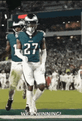 a group of football players are running on a field and one of them has the number 27 on his jersey .