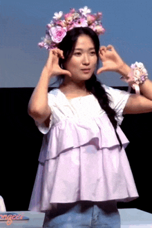 a woman wearing a flower crown making a heart shape with her hands
