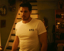 a man wearing a white r.p.d. t-shirt stands in front of some stairs