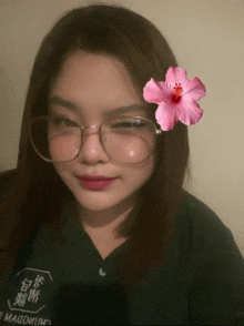 a woman wearing glasses has a pink flower in her hair and a shirt with chinese writing on it