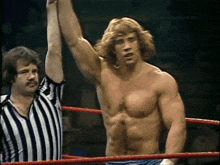 a referee holds up a shirtless wrestler 's arm in a ring