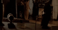 a woman is standing in front of a fireplace in a dark room in front of a mirror .