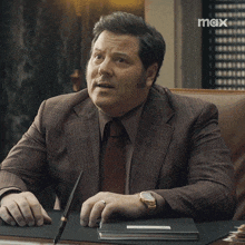 a man in a suit and tie is sitting at a desk asking what does that mean
