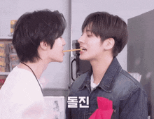 two young men are eating a stick with korean writing on the bottom right corner