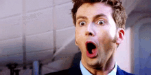 a man in a suit is making a surprised face with his mouth open .