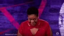 a woman in a red dress is clapping her hands while sitting in front of a nbc wall