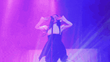 a woman singing into a microphone in front of a purple light