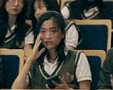 a girl in a school uniform is sitting in a classroom with a cell phone in her hand .