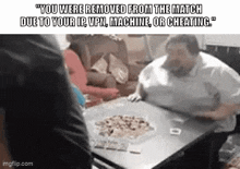 a man is sitting at a table with a pizza on it and a group of people are sitting on a couch .