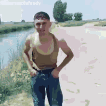a man in a tank top and jeans is standing on a dirt road .