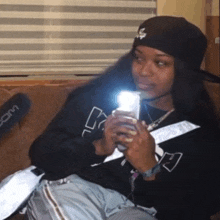 a woman sitting on a couch holding a cell phone in front of a zoom microphone