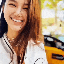 a woman with a pearl necklace smiles in front of a yellow vehicle