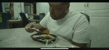 a man in a white shirt is sitting at a table eating a tray of food