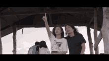 a man and a woman are standing under a wooden structure and the woman is wearing a shirt that says " torment " on it