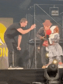a man in a black shirt is standing on a stage next to a man in a cowboy hat .