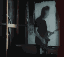 a shadow of a man playing a guitar is projected on a wall