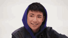 a young boy wearing a purple hoodie and a black jacket is smiling .