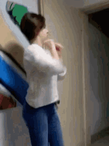 a woman in a white shirt and blue jeans is standing in front of a wall with boxes on it .