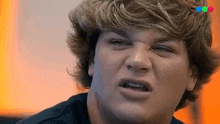 a young man with blonde hair is making a funny face while looking at the camera .