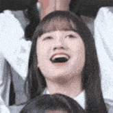 a close up of a woman laughing with her mouth open while sitting in a crowd .