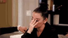 a woman is sitting on a couch with her hand on her face .