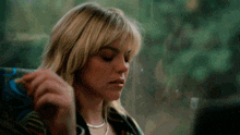 a woman with blonde hair and bangs is eating a french fry while sitting in front of a window .