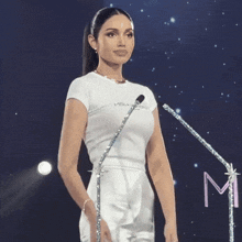 a woman in a white dress is standing in front of a microphone with the letter m on it