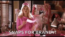 a woman in a pink dress is holding a piece of paper and says snaps for brandy !