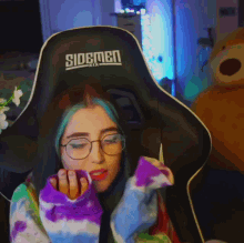 a girl with blue hair is sitting in a sidemen gaming chair