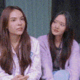 two women are sitting next to each other on a couch and looking at something .