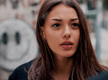 a close up of a woman 's face with a smiley face on the wall behind her