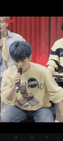 a man with blue hair is singing into a microphone while wearing a yellow shirt .