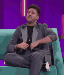 a man in a suit is sitting on a teal couch .