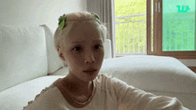 a woman with blonde hair is sitting on a bed in front of a window with a green w on it
