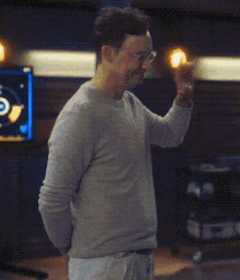 a man wearing glasses and a grey sweater is standing in a room with green lights coming out of his body .