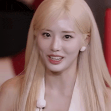 a close up of a woman with long blonde hair wearing a white shirt and earrings .