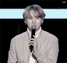 a young man in a white jacket is holding a microphone to his mouth .