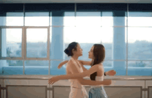 two women are hugging each other in front of a window in a dance studio .