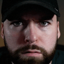 a close up of a man 's face with a beard wearing a black hat