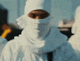 a man with a white scarf around his head looks at the camera