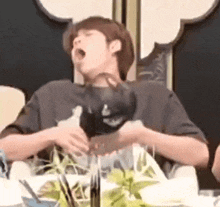 a man is sitting at a table with his mouth open holding a hat .