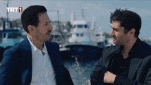 two men are talking in front of a boat with trt1 written on the bottom
