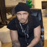 a man with dreadlocks is sitting in a chair wearing a black beanie and a necklace .
