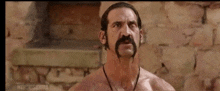 a shirtless man with a mustache is standing in front of a brick wall