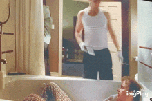 a man is laying in a bathtub while another man stands behind him