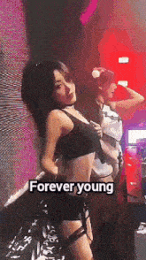 a woman in a crop top and shorts is dancing in a club with the words forever young above her