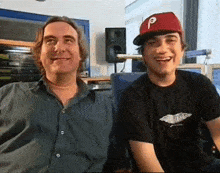 a man and a boy are sitting next to each other and the boy is wearing a hat with the letter p on it