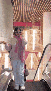 a woman wearing sunglasses and a pink scarf is riding an escalator in a store .
